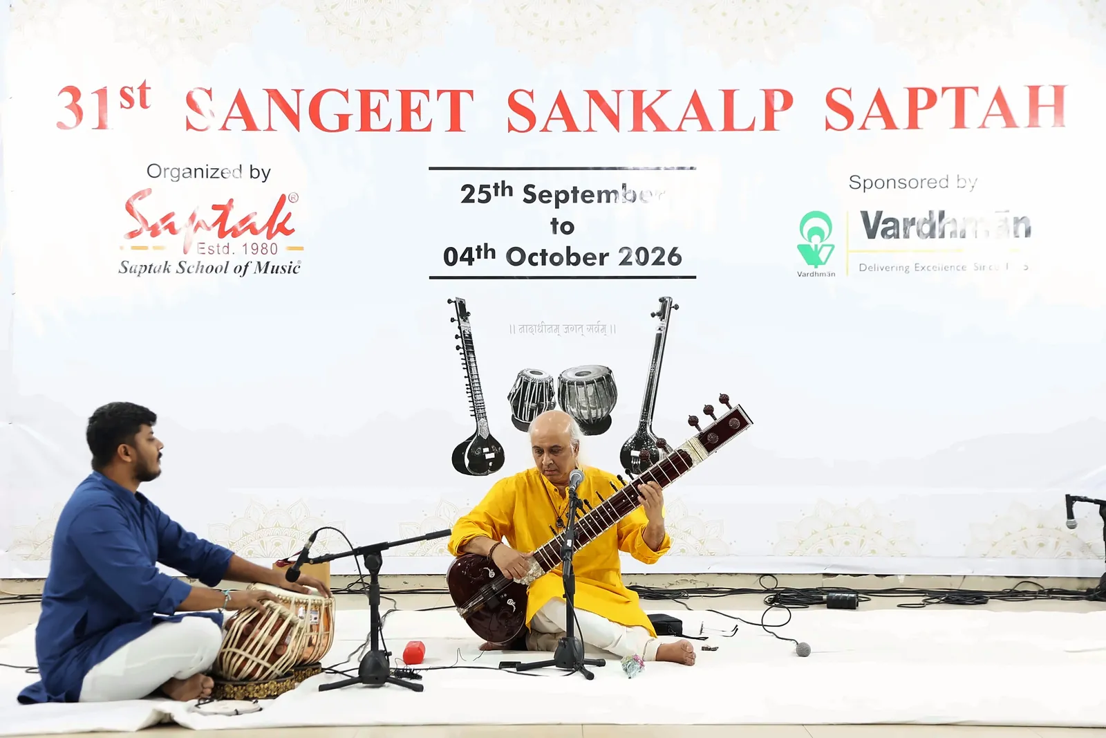 Vatsal Dave playing sitar in a yellow kurta with Riddhish Vora on tabla, under the 31st Sangeet Sankalp Saptah banner of Saptak School of Music, Ahmedabad