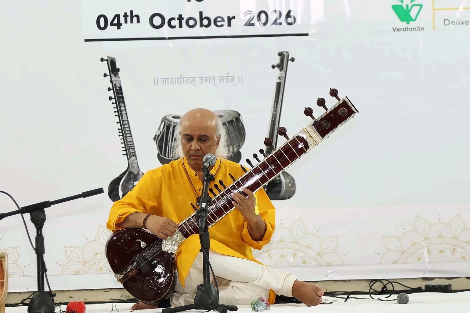Vatsal Dave playing sitar beneath the festival banner reading 04th October 2026, with sitar and tabla artwork behind him