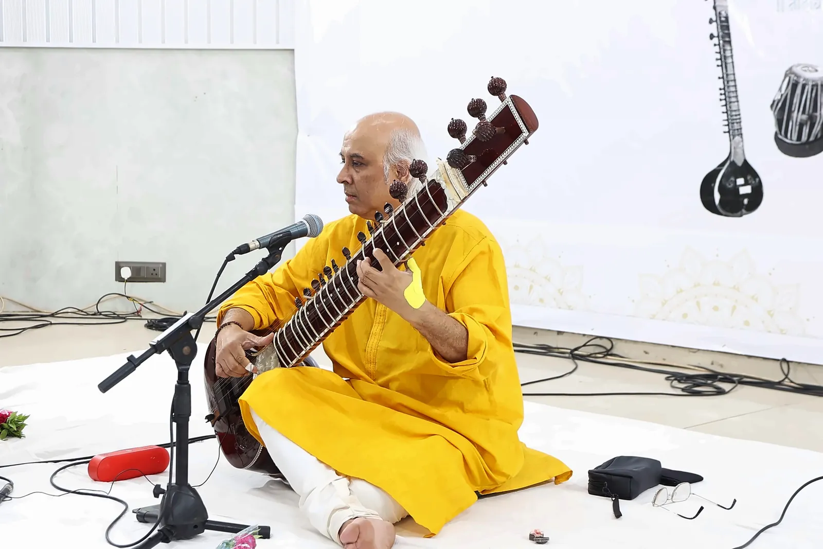 Side view of Vatsal Dave seated on stage playing sitar, with a microphone on a boom stand