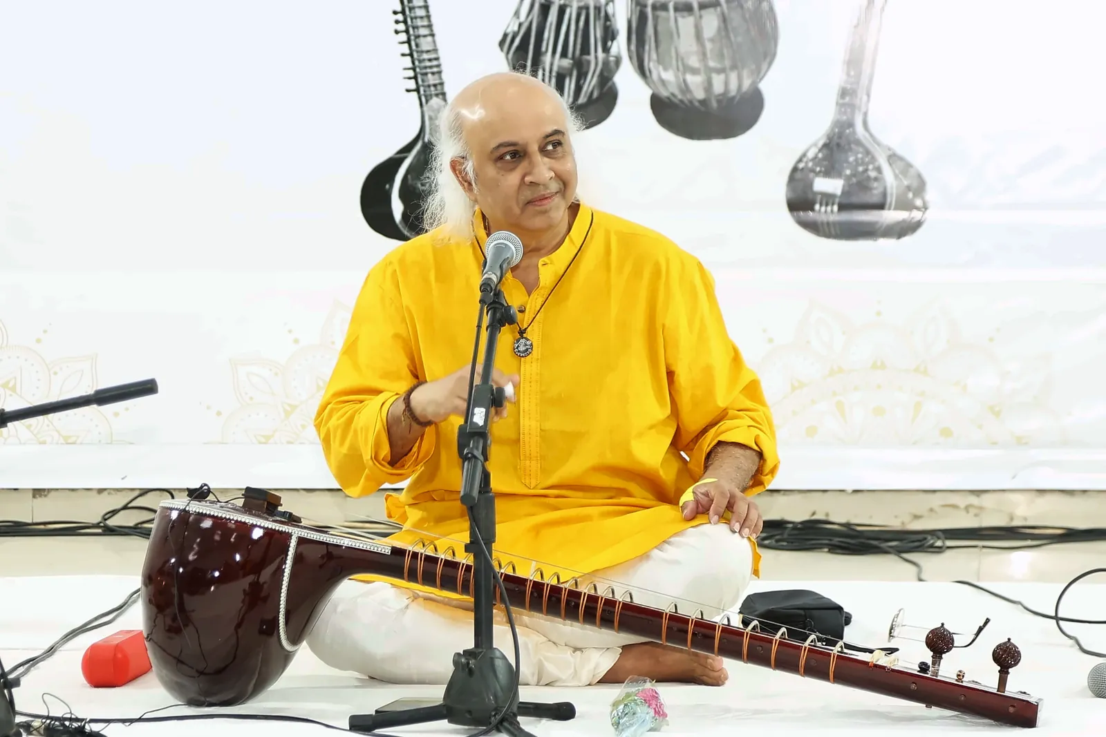 Vatsal Dave smiling and looking to the side between pieces, the sitar resting across the floor in front of him